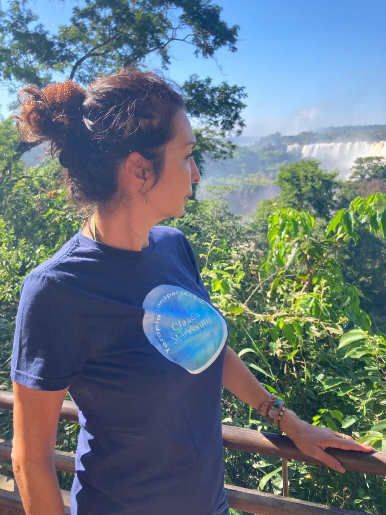 Claudia Morassutti disfrutando de la naturaleza frente a una cascada, representando la conexión con el entorno natural.
